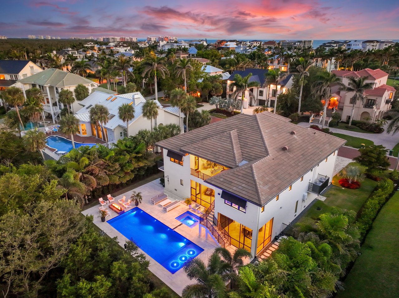 Aerial view of a modern home with an illuminated pool and spa at dusk.