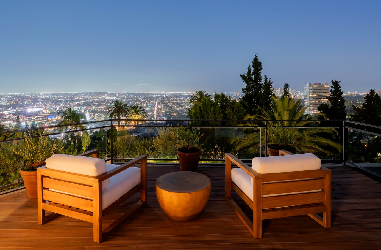 Wood deck seating overlooks a brightly lit city skyline at twilight.