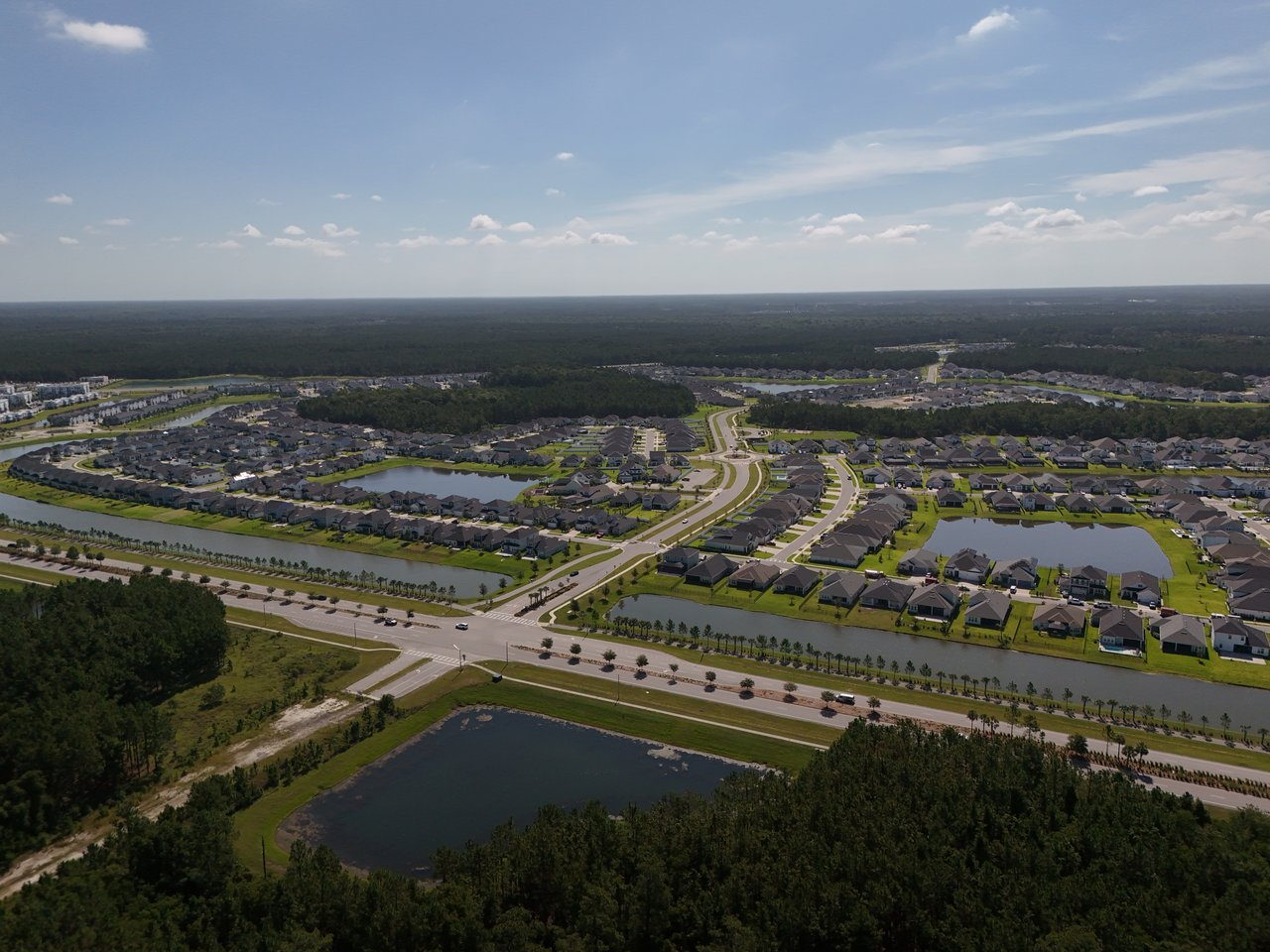 Aerial view of a residential community with curving streets, ponds, and surrounding woodland.