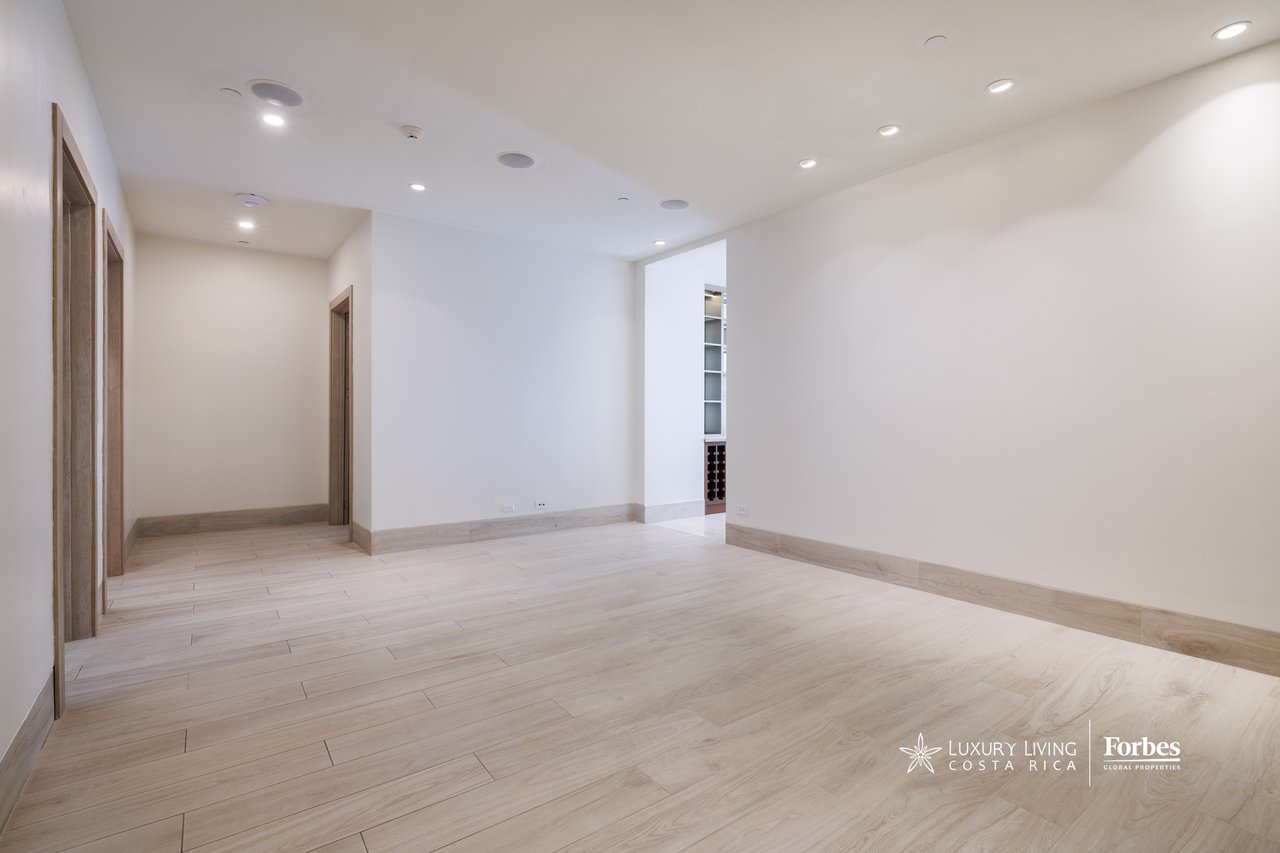 Empty apartment room with pale tile flooring, recessed lights, and a built-in wine rack.