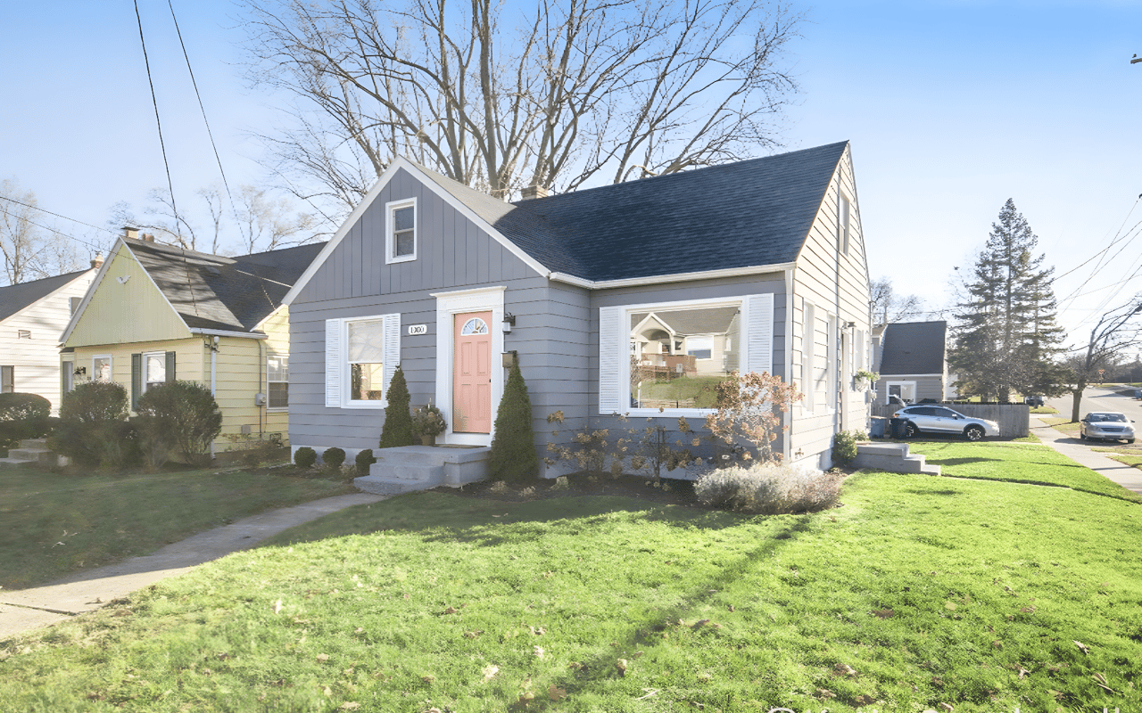 Gray gable-front house with white trim, a pink front door, and a sunny front lawn.
