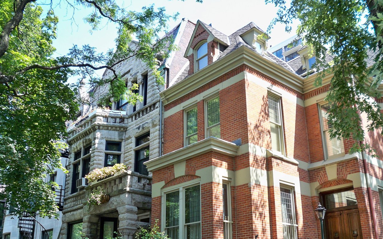 Multi-story red brick residence with pale stone trim, framed by leafy trees.