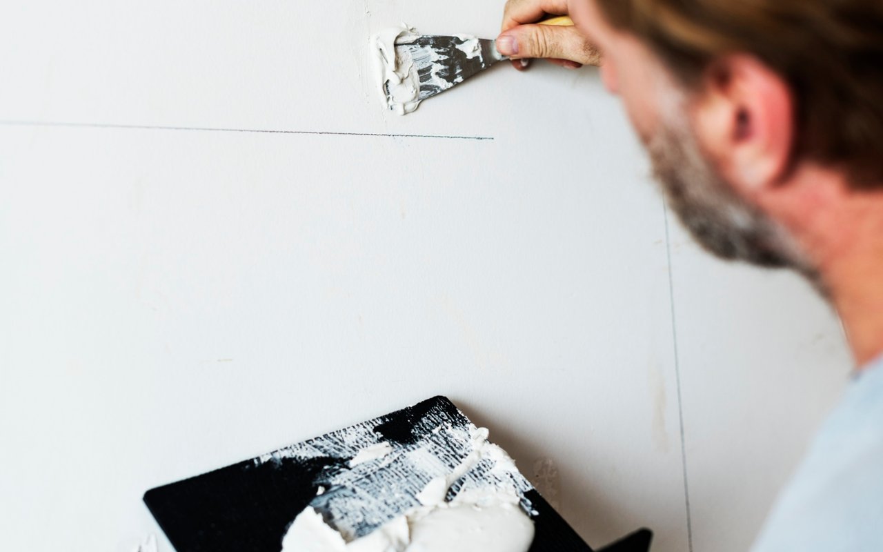 A man spreads joint compound over a seam on an interior wall.