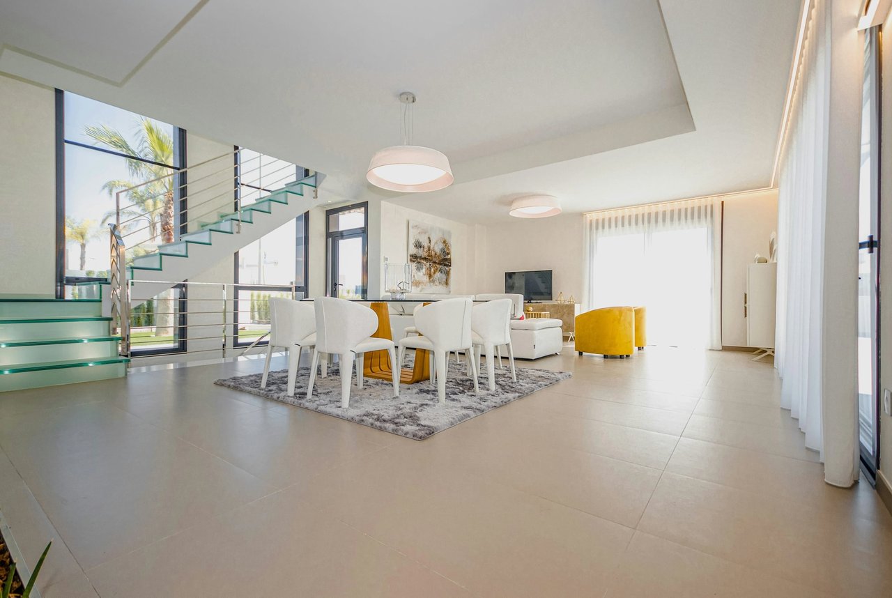 Modern open-plan living and dining room with a glass staircase and yellow accent chairs.