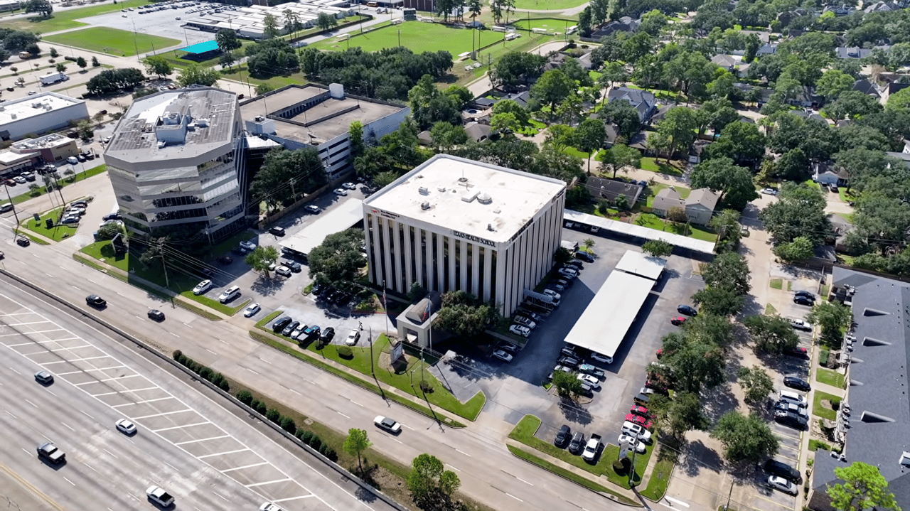 Aerial view of Texas Health School, with adjacent office building, parking lots, and highway.