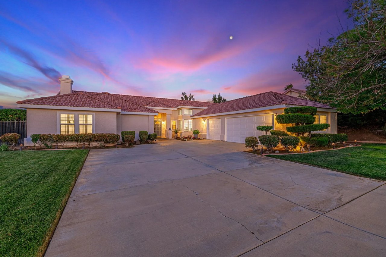Single-story stucco home with tile roof and three-car garage beneath a colorful dusk sky.