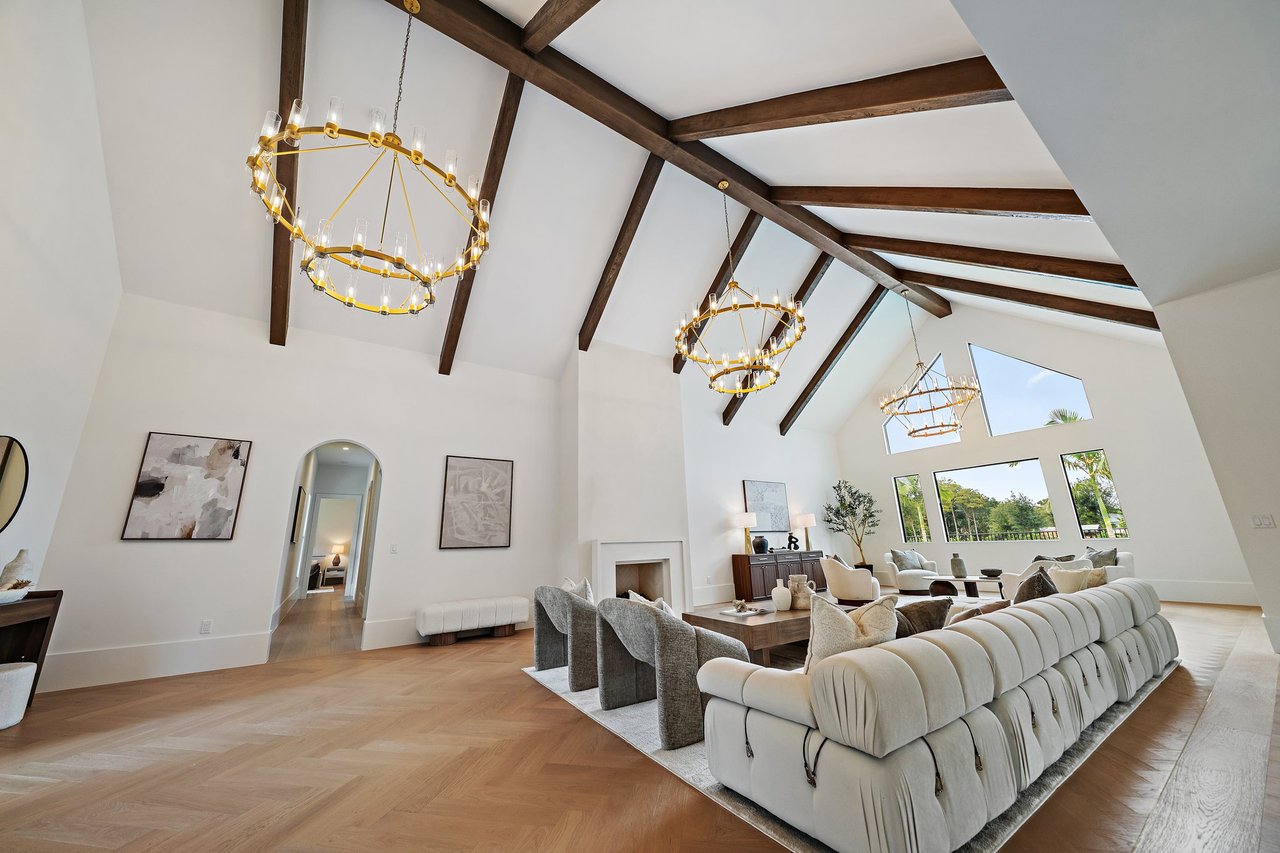 Living room with vaulted beam ceiling, gold chandeliers, fireplace, and herringbone floors.