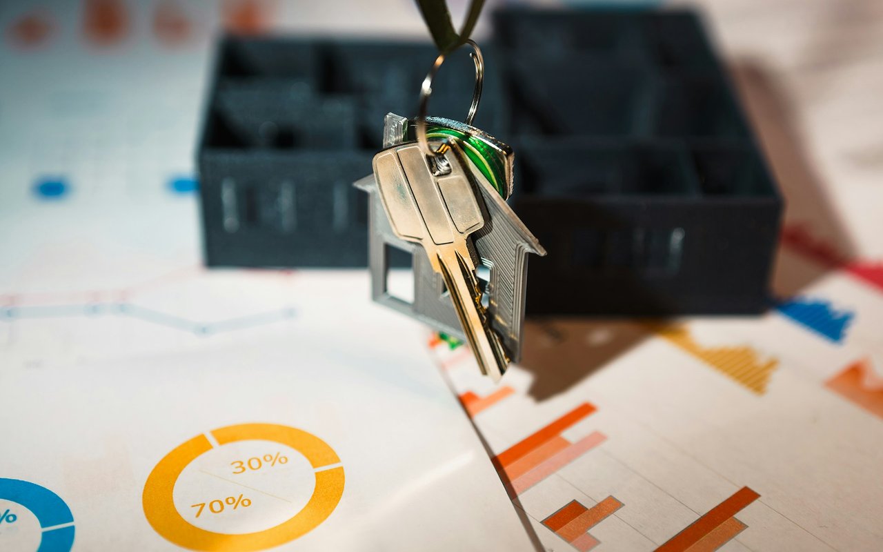 House-shaped keychain and keys over printed real estate market charts.