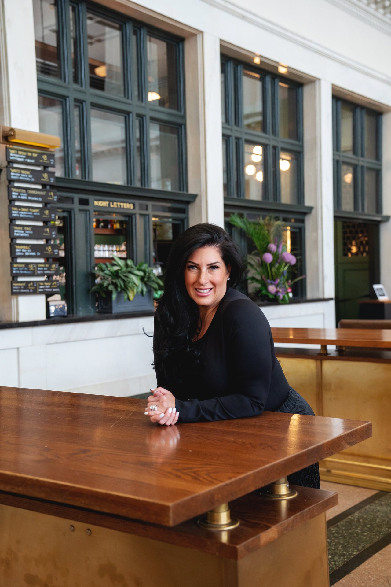 Rachel Sartin leans on a wooden counter in a bright interior.