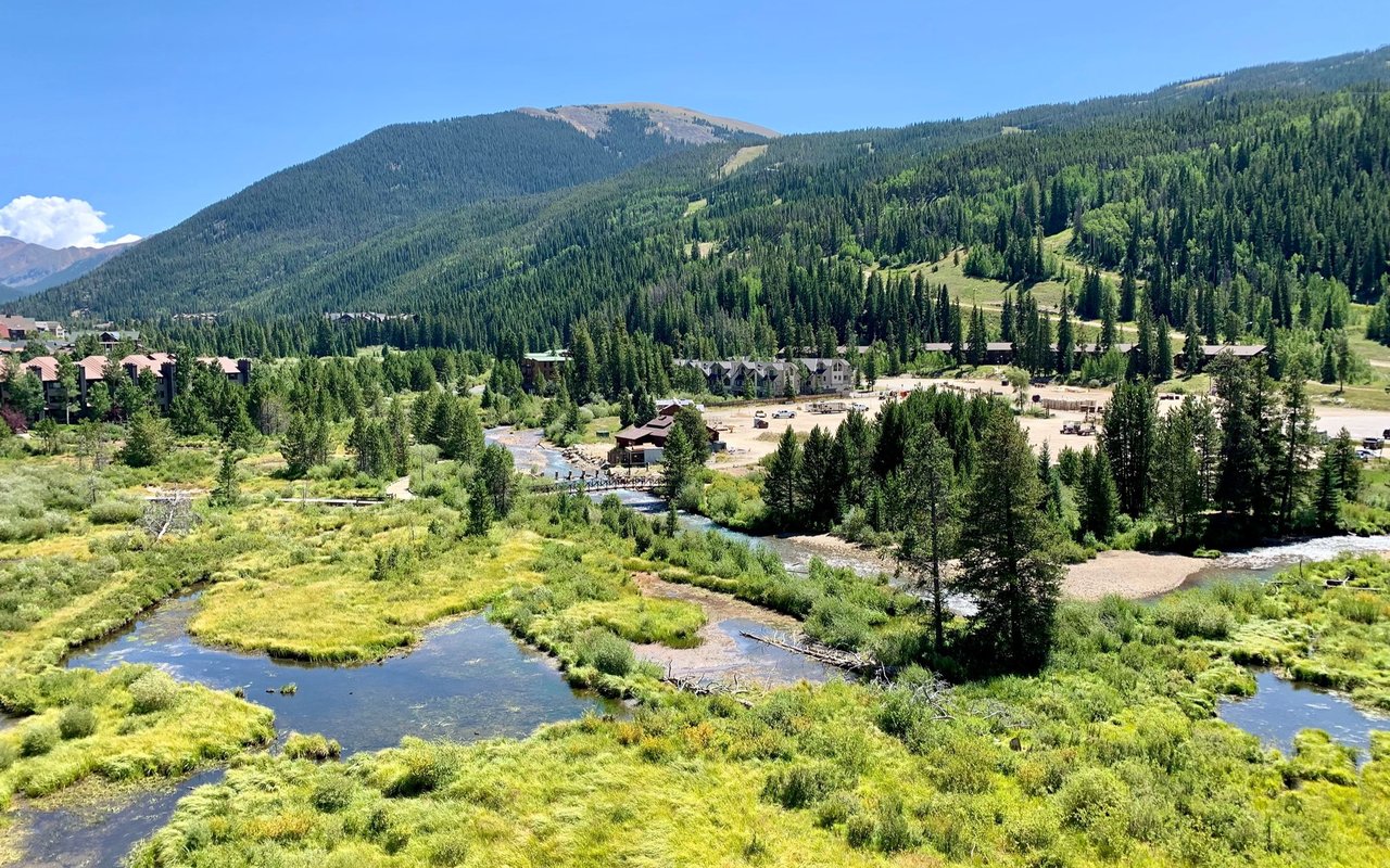 Keystone mountain valley with resort buildings, forested slopes, and a stream winding through green wetlands.