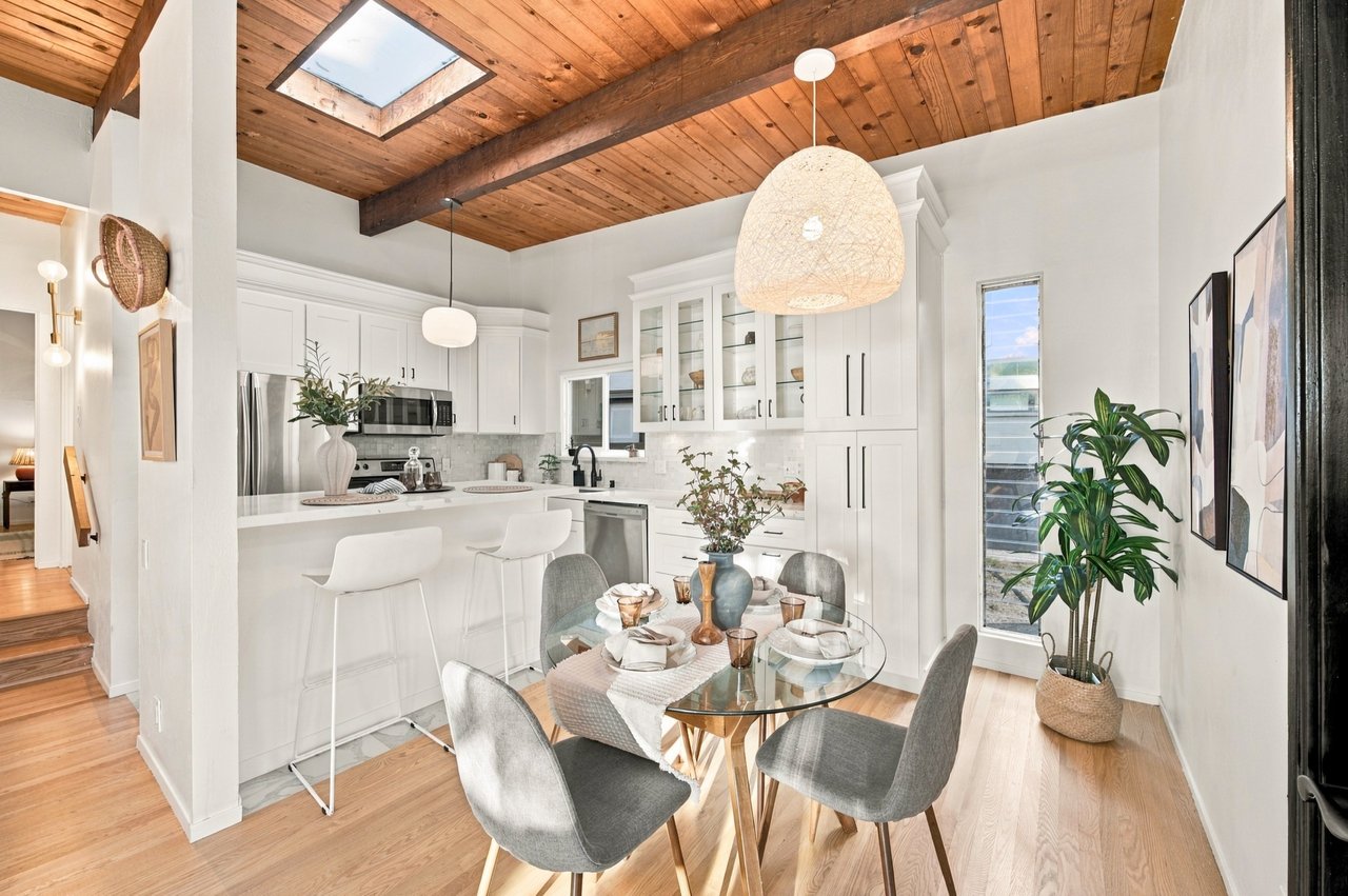 Bright kitchen and dining area with white cabinetry, a wood-beamed ceiling, and a glass dining table.