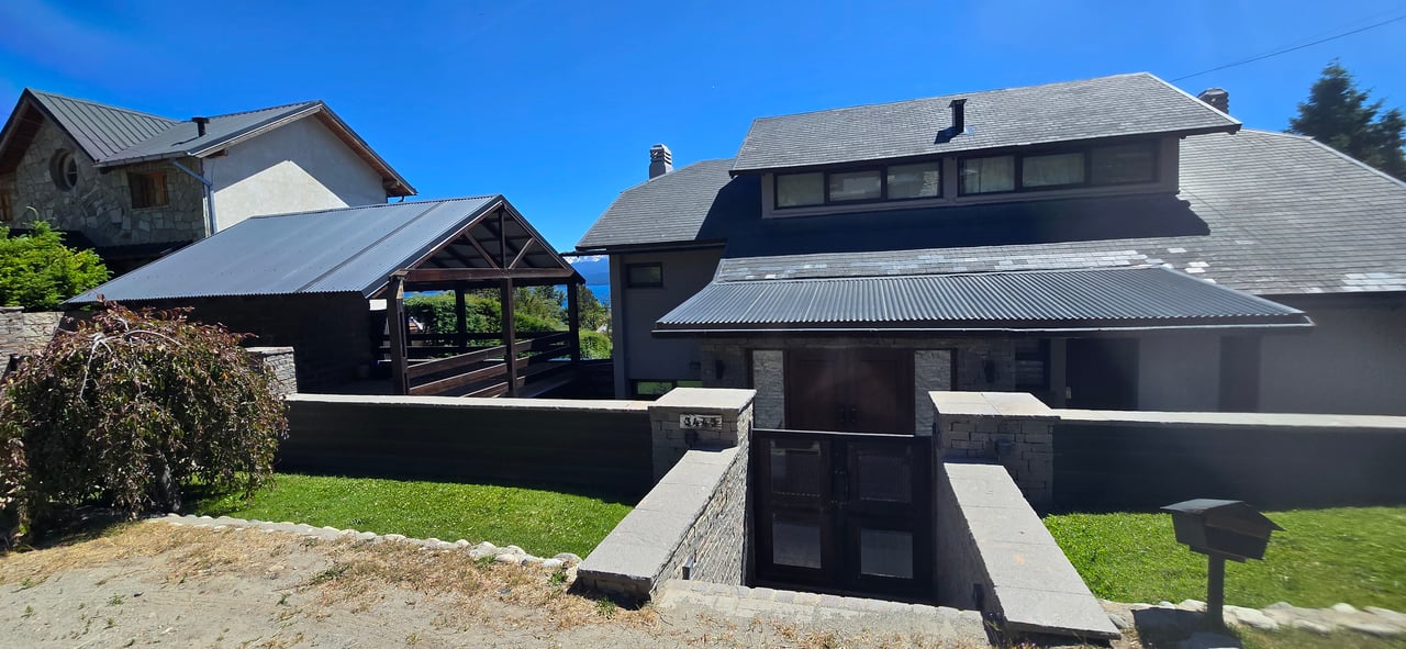 Two-story house with gray roofs, stone accents, and a gated entrance beside a covered carport.