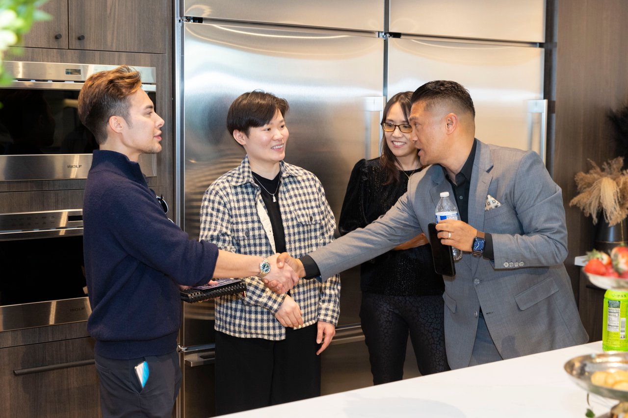 Four people socialize in a modern kitchen as two men shake hands.