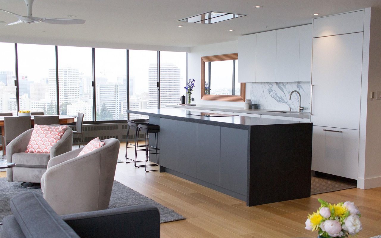 Open-plan kitchen with a dark island, white cabinets, and floor-to-ceiling windows overlooking the city.