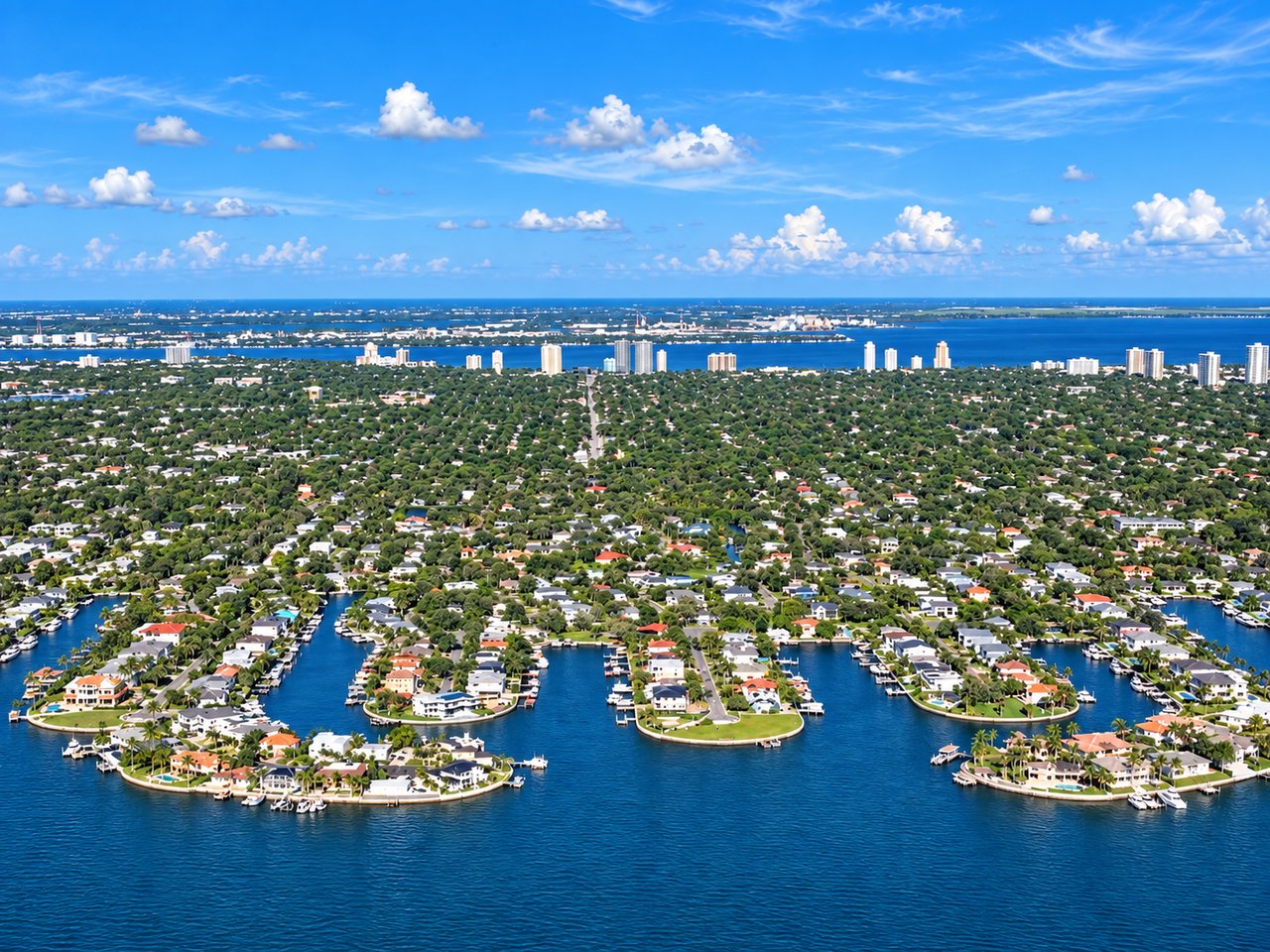 Waterfront neighborhood with canal-side homes and boats, backed by distant high-rises.