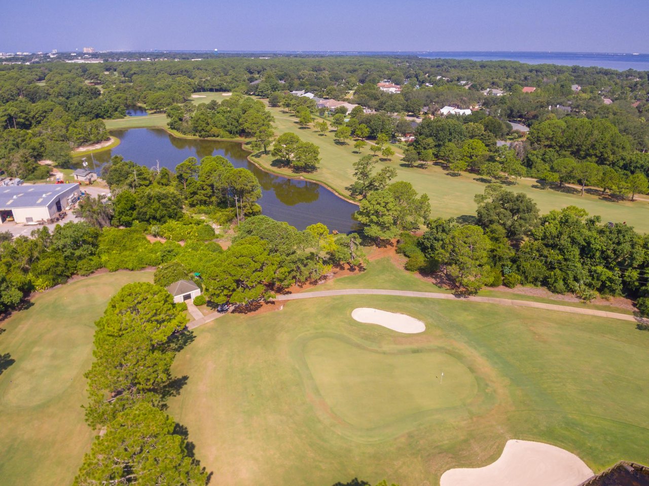 Golf course with sand bunkers and a pond, with homes and water in the distance.