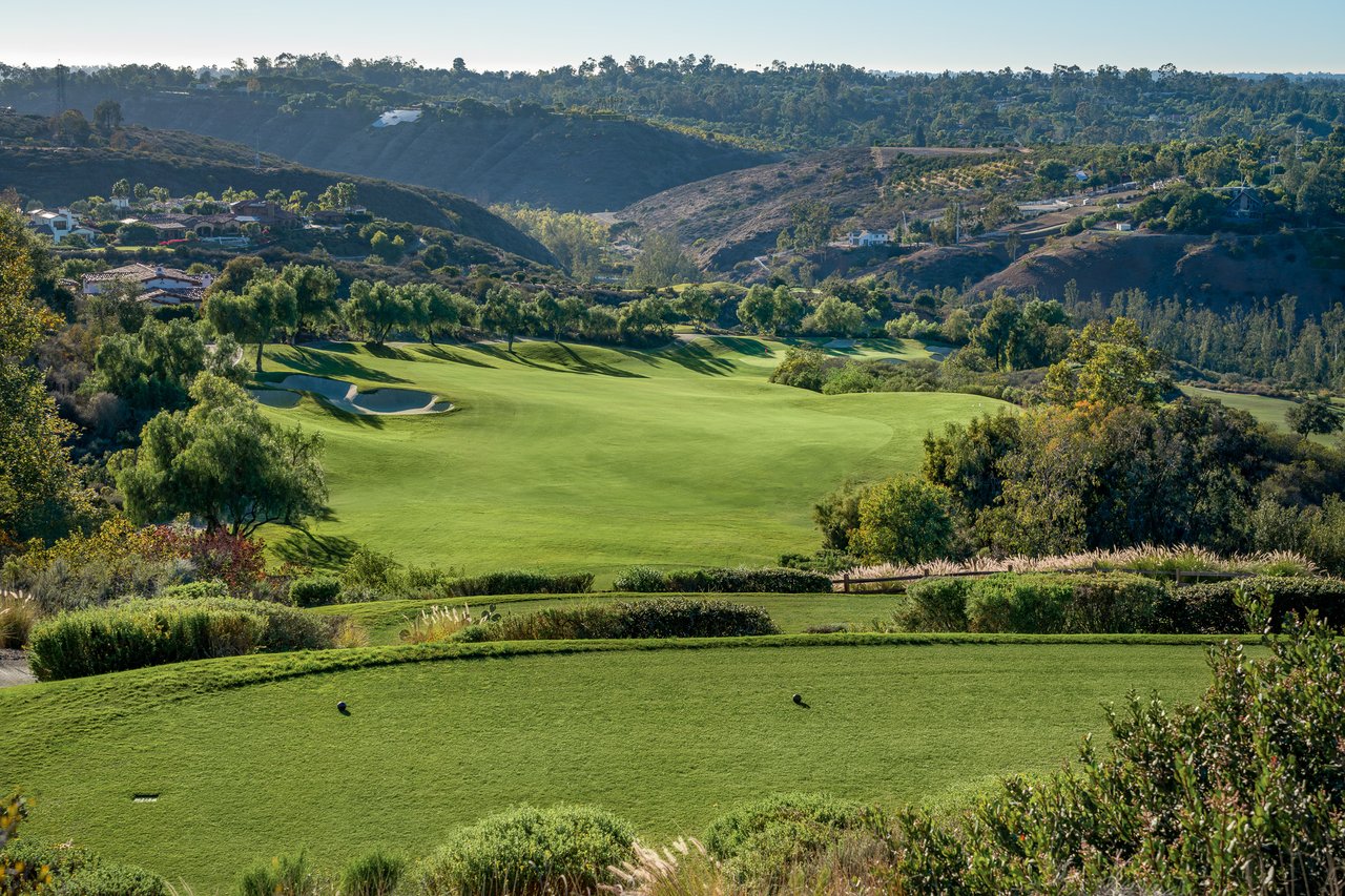 Golf course with sand bunkers and wooded hills dotted with homes.