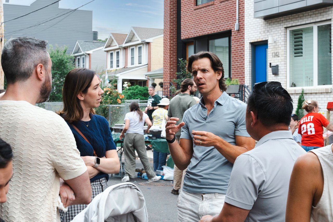 Neighbors talk at an outdoor block party on a residential street lined with row houses.