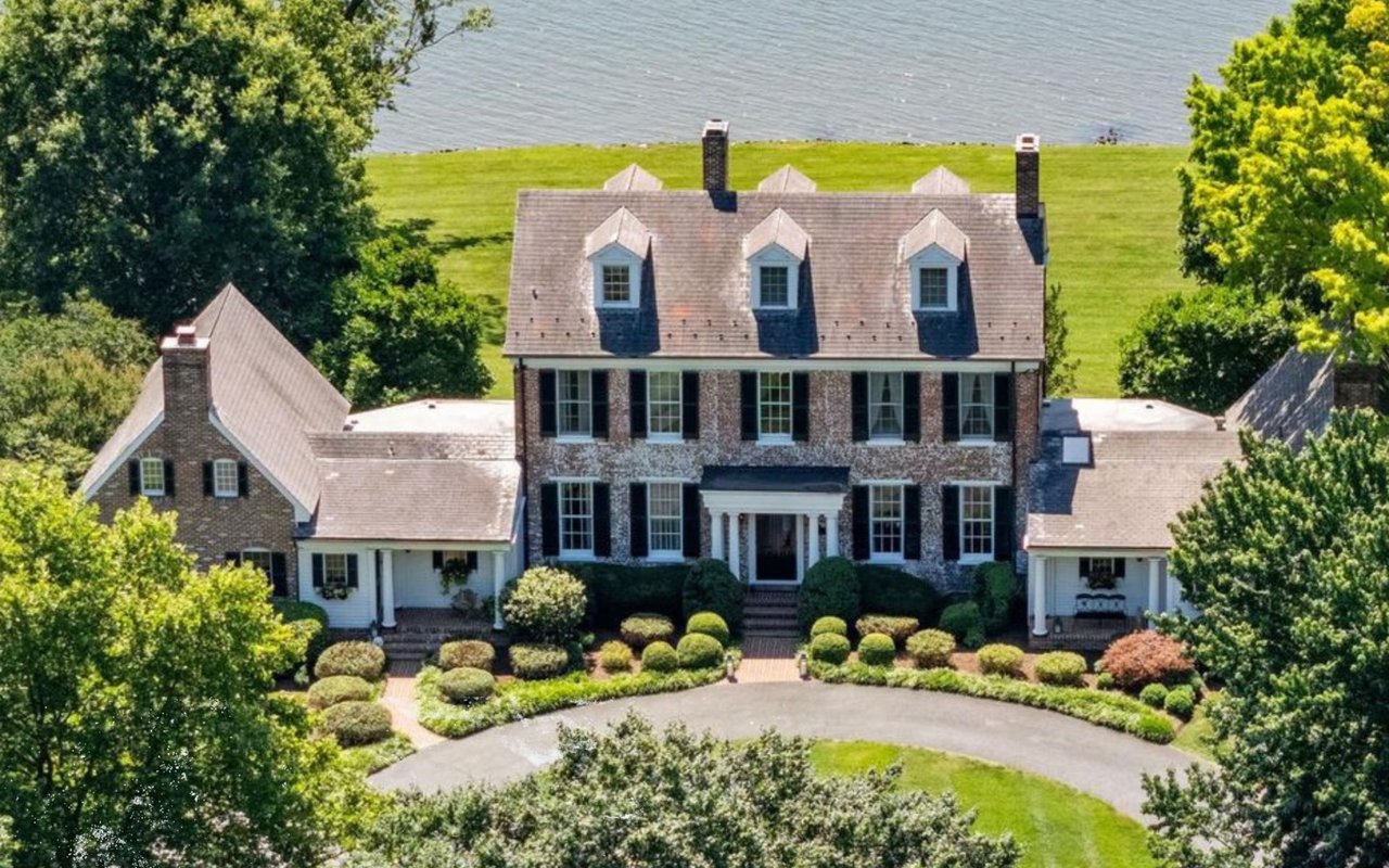 Brick waterfront home with three dormers, landscaped grounds, and a circular driveway.
