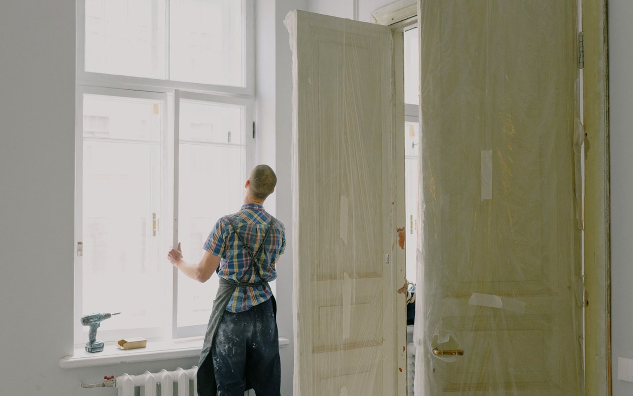 Renovation worker preparing a bright room, with doors covered in protective sheeting.