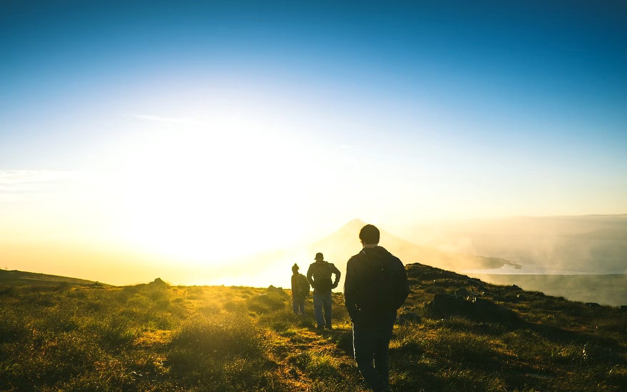 Three hikers walk along a mountain ridge toward a sunlit peak.
