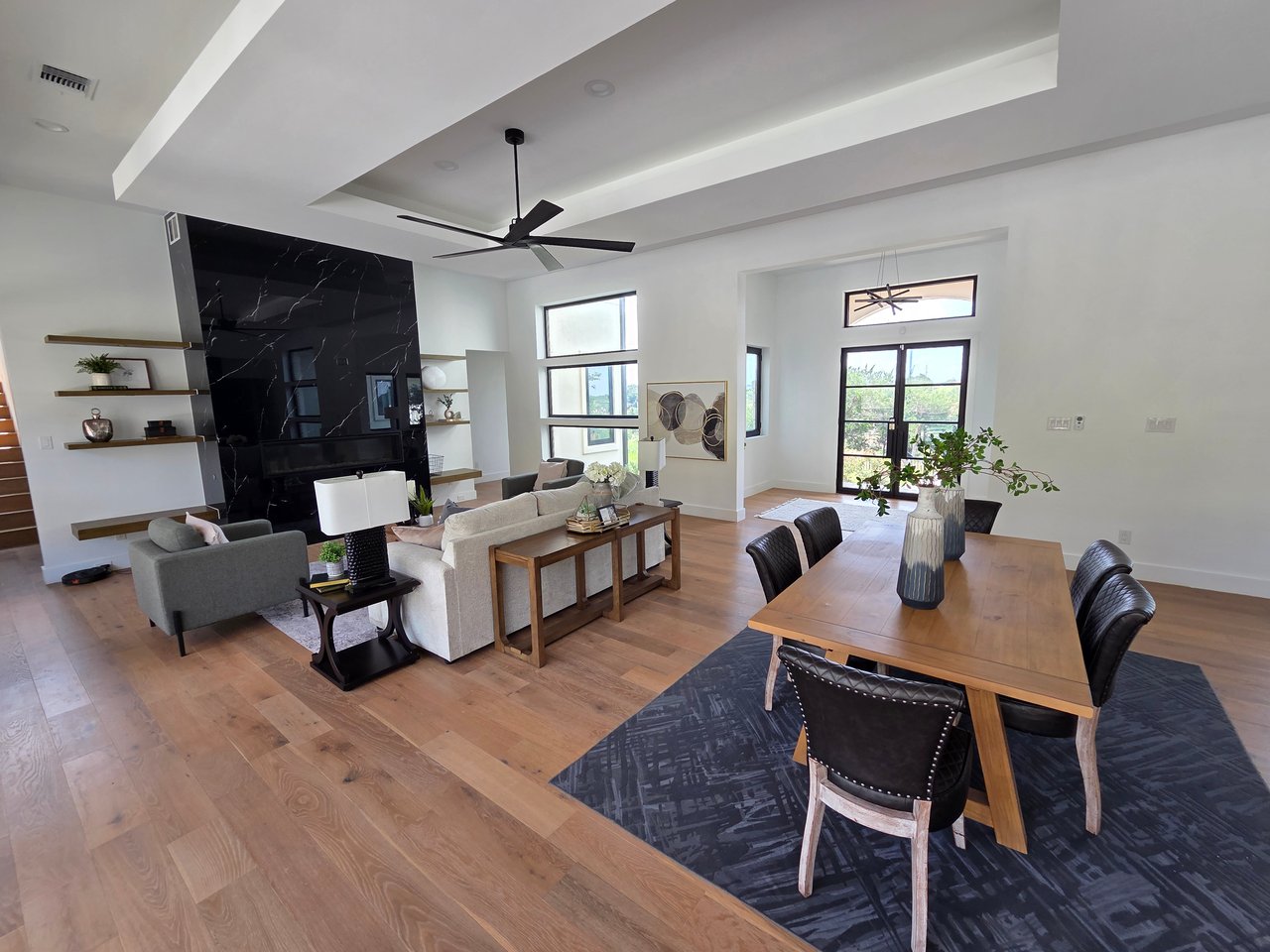 Open-plan living and dining room with a dramatic black marble fireplace wall and warm wood floors.