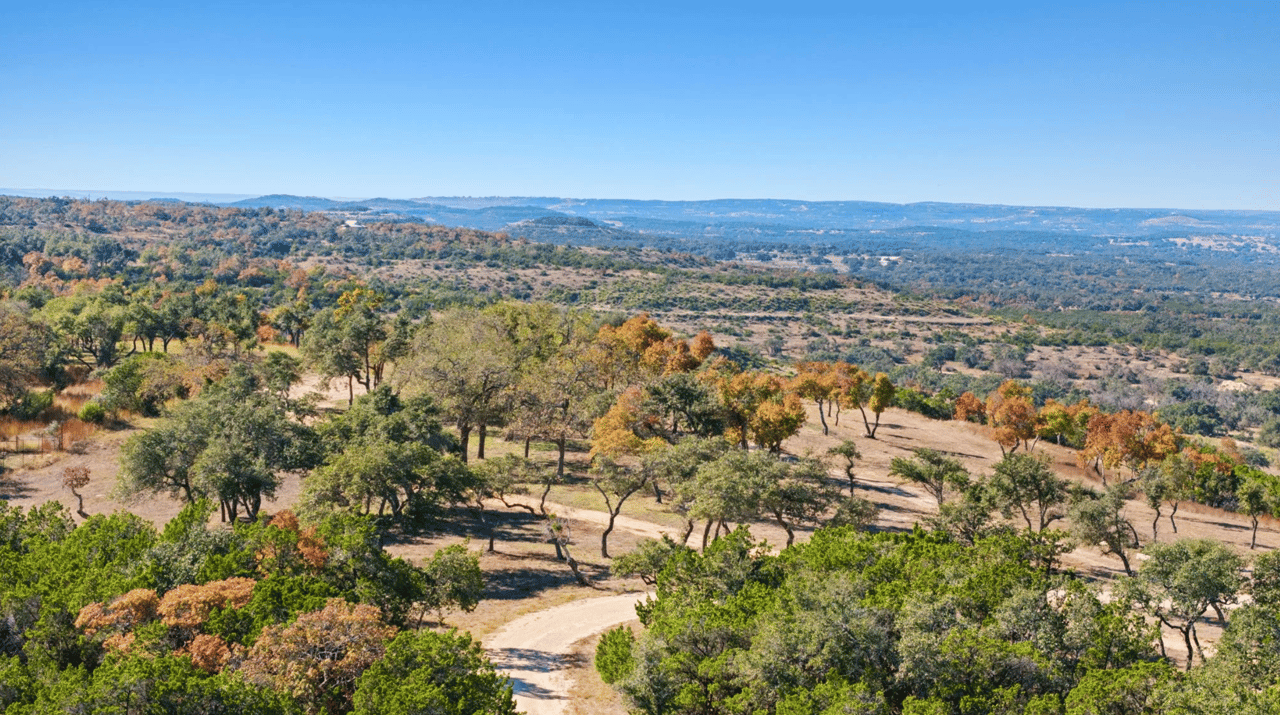 Rolling ranch land with autumn-colored trees and a winding dirt road.