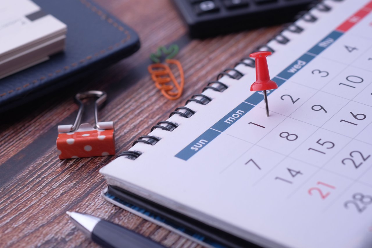 Calendar with a red pushpin marking the first day, beside a polka-dot binder clip and pen.