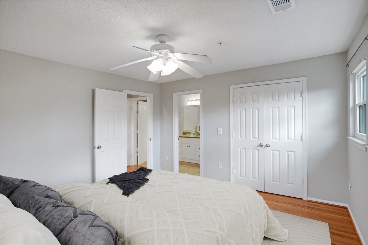 Bedroom with a white quilted bed, ceiling fan, double closet doors, and an adjoining bathroom doorway.