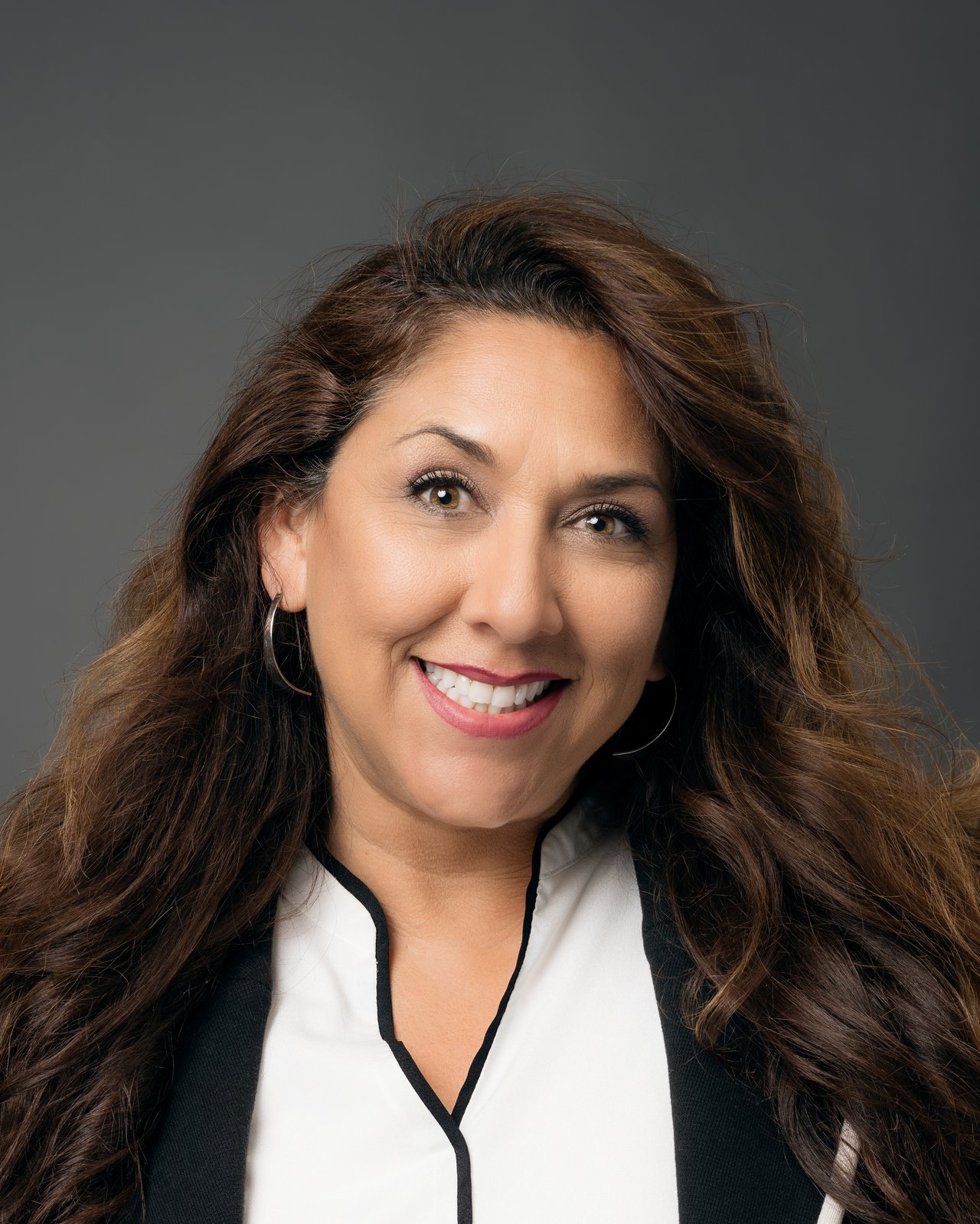 Melanie Block smiling in a black-and-white blouse against a gray background.