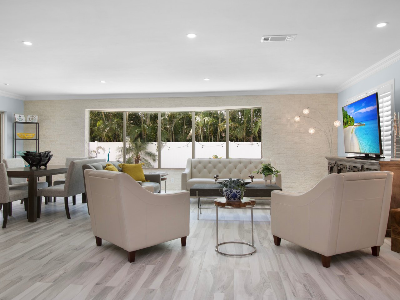 Living room with cream seating, pale stone walls, and large windows overlooking tropical greenery.