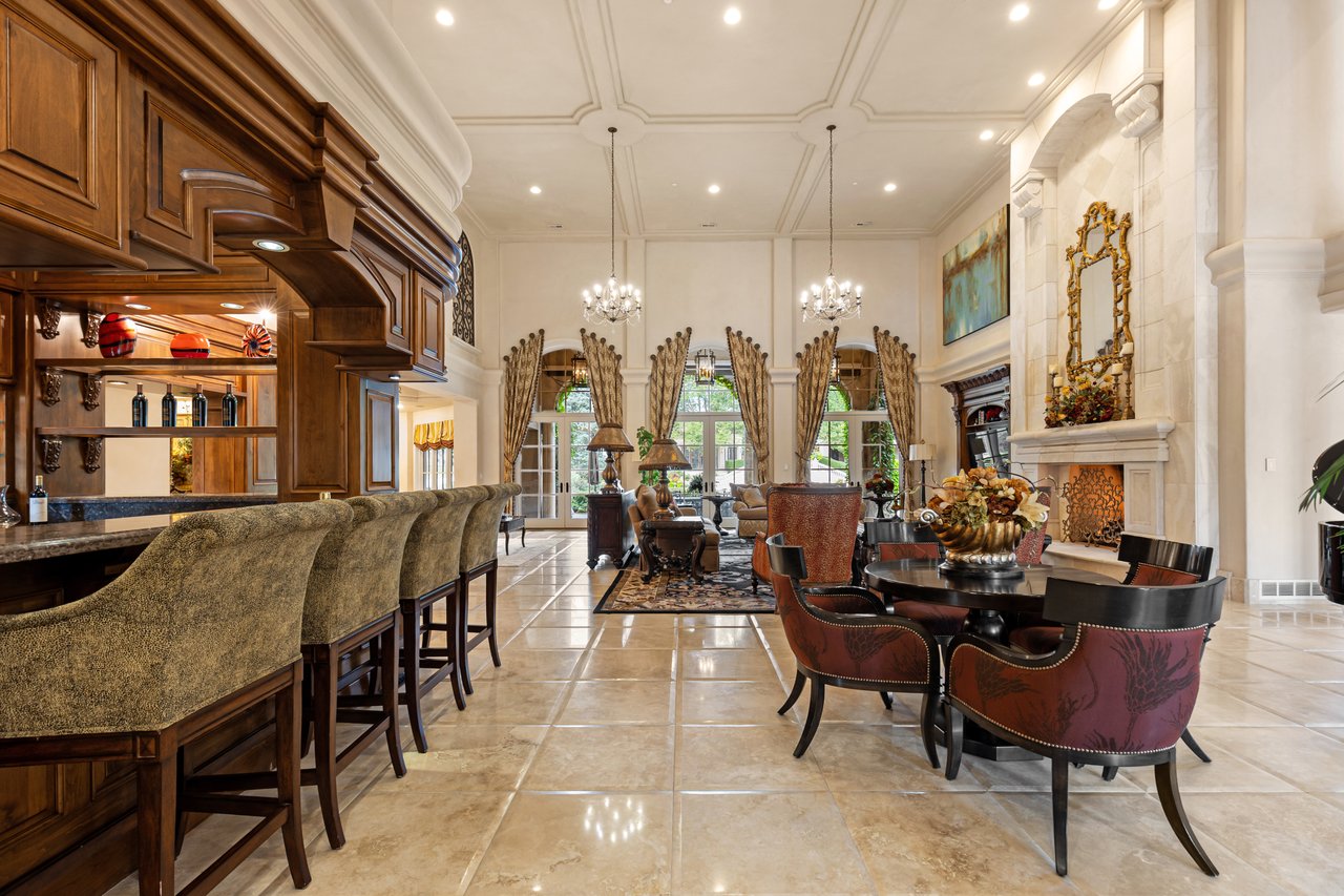 Estate great room with a built-in wood bar, tall windows, and a large stone fireplace.