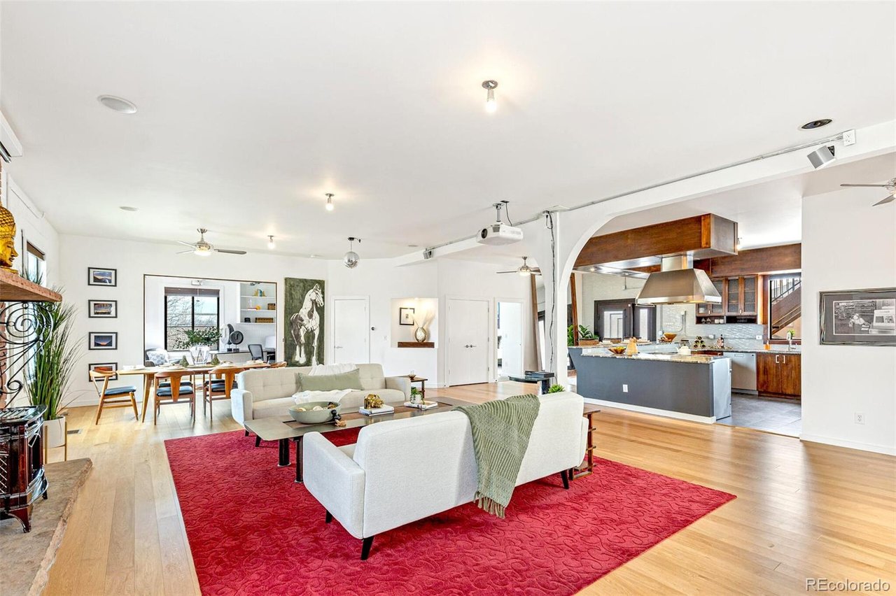 Open-plan living room with white sofas, a red rug, dining area, and wood-accented kitchen.