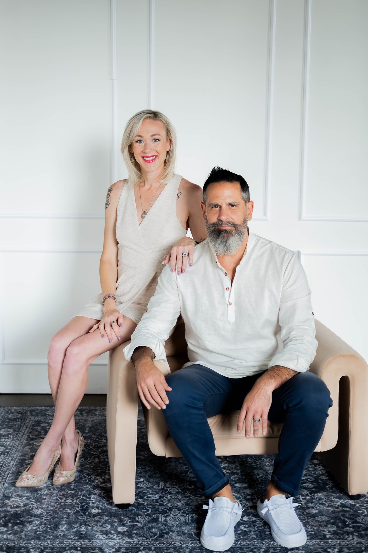 Brittany and Bryan Stewart pose together, with Brittany standing beside Bryan in a beige armchair.
