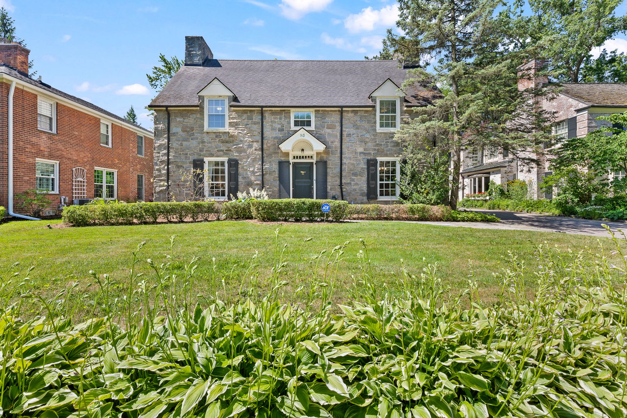 Exterior of a stone Colonial home with a manicured front lawn, mature trees, and landscaped front yard in Grosse Pointe Farms.