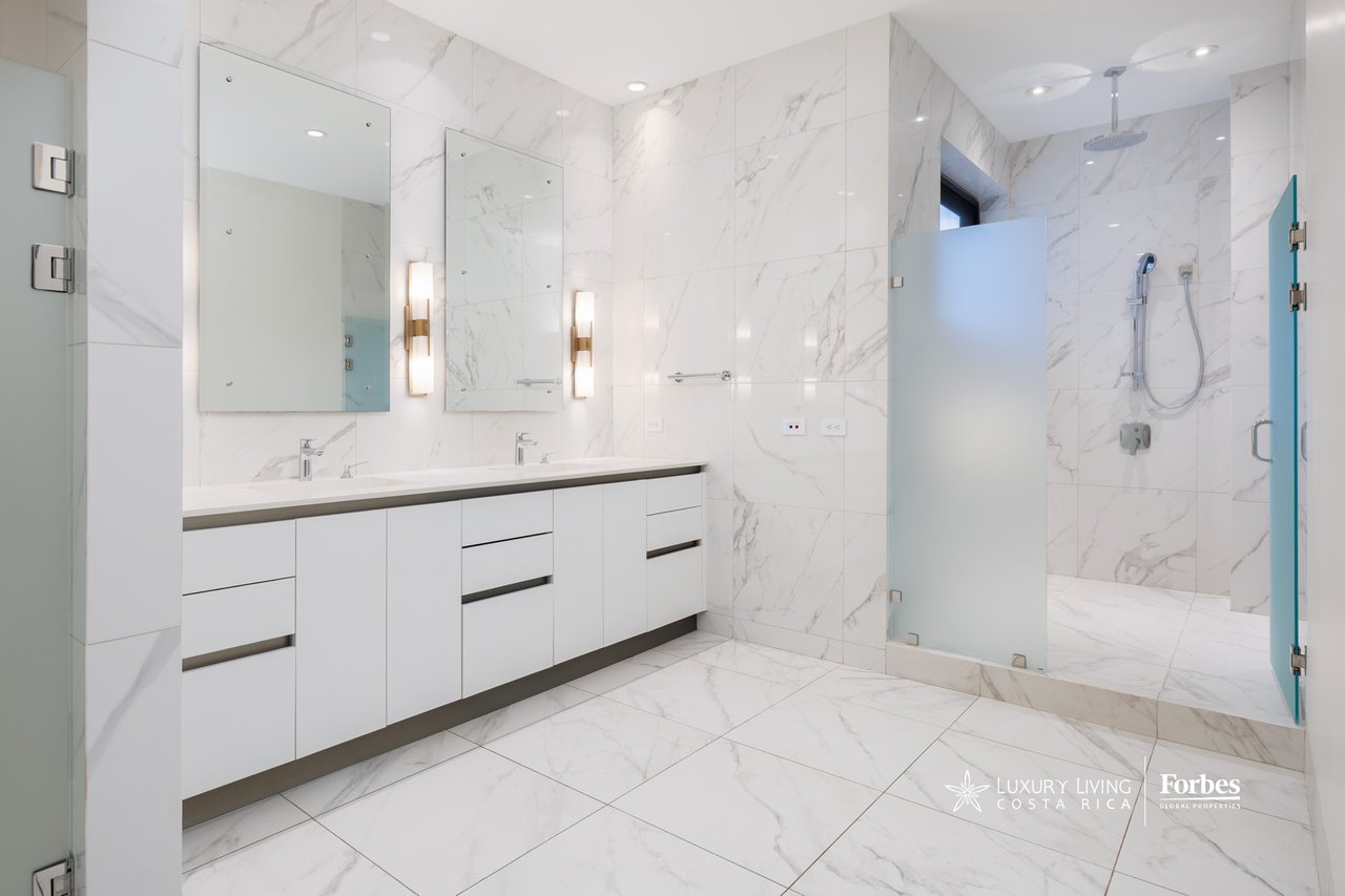 Modern marble-tiled bathroom with a double vanity and glass-partitioned walk-in shower.