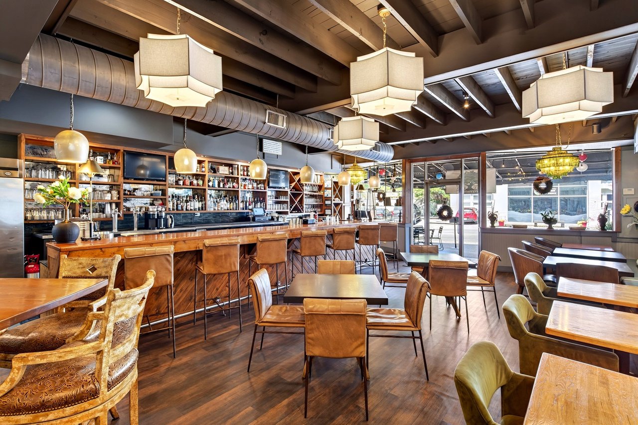 Restaurant interior with a long wood bar, leather seating, and large front windows.