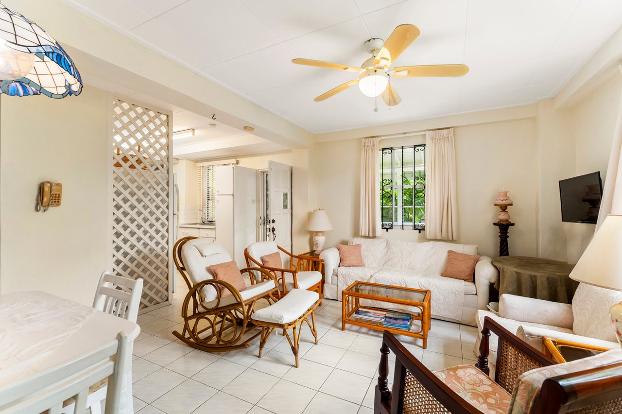 Furnished living room with white sofas, rattan rocking chairs, and a glass-top coffee table.