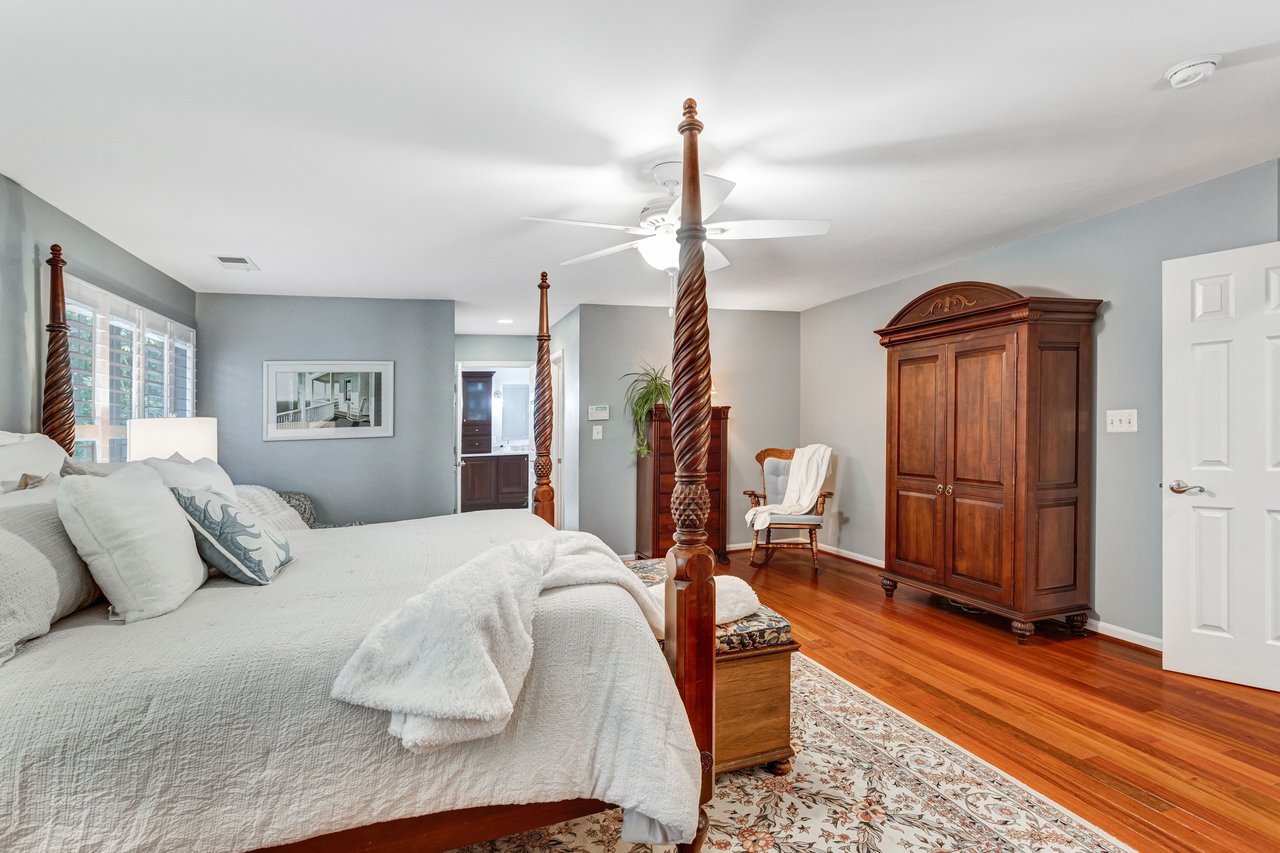 Bedroom with a four-poster bed, polished wood floors, and a large wooden armoire.