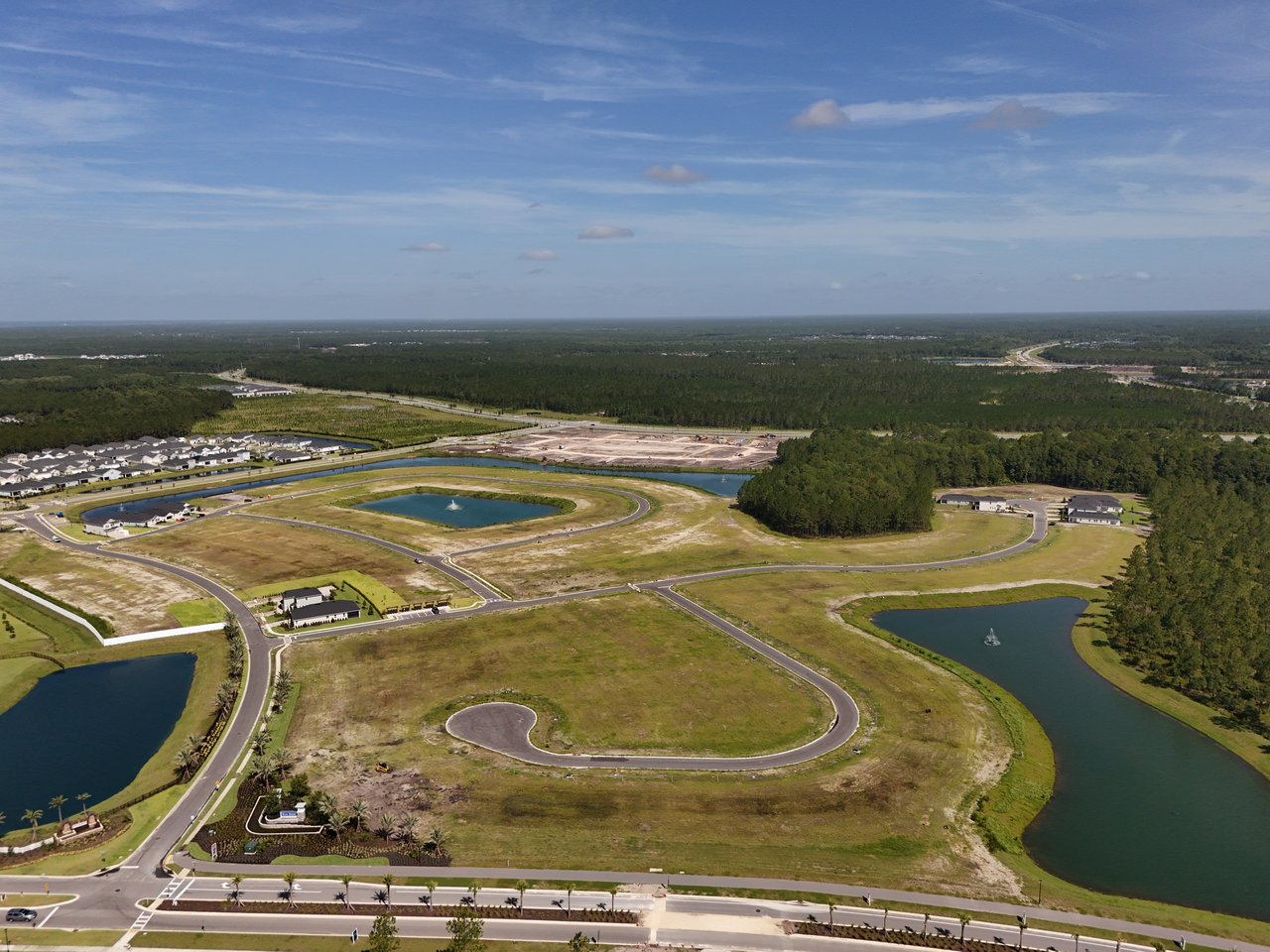 Aerial view of a residential development with curving roads, ponds, vacant lots, and surrounding woods.