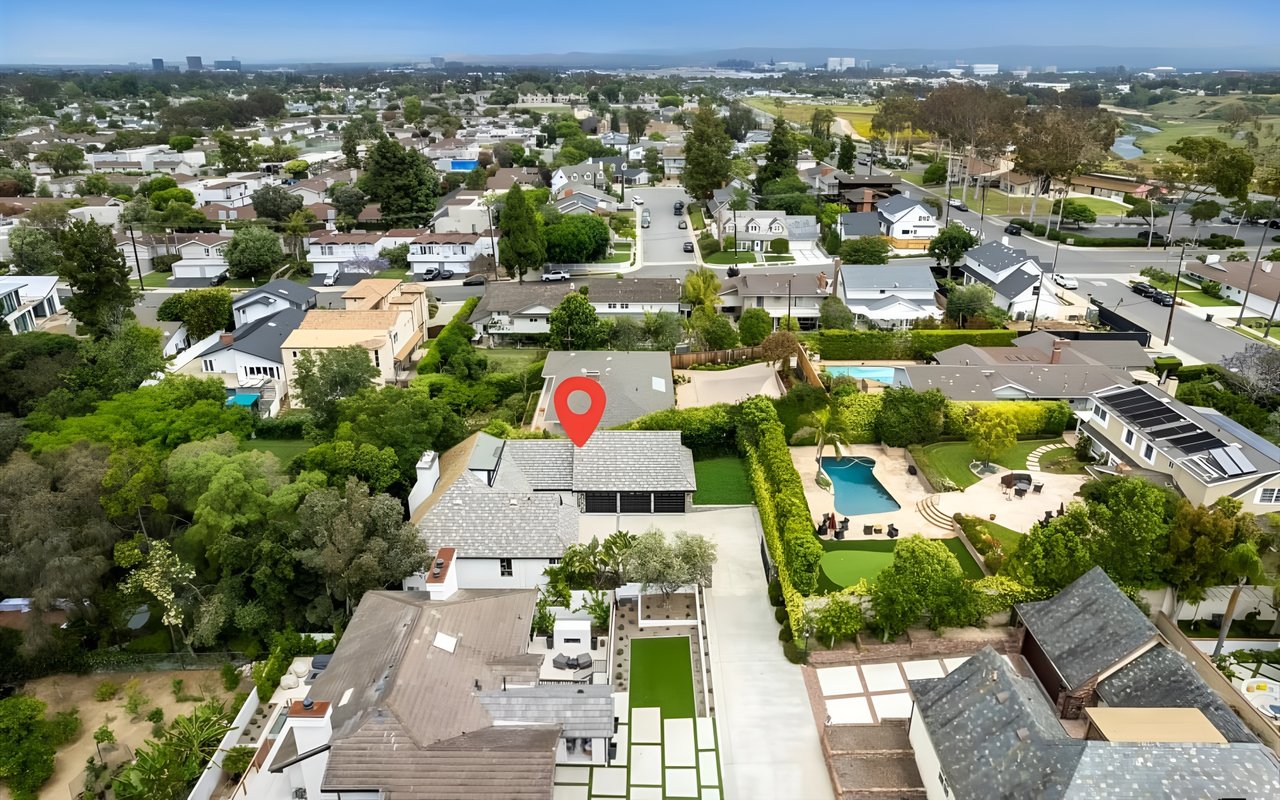 An aerial view of a suburban neighborhood, with a red pin marking a gray house with a two-car garage and a large backyard.