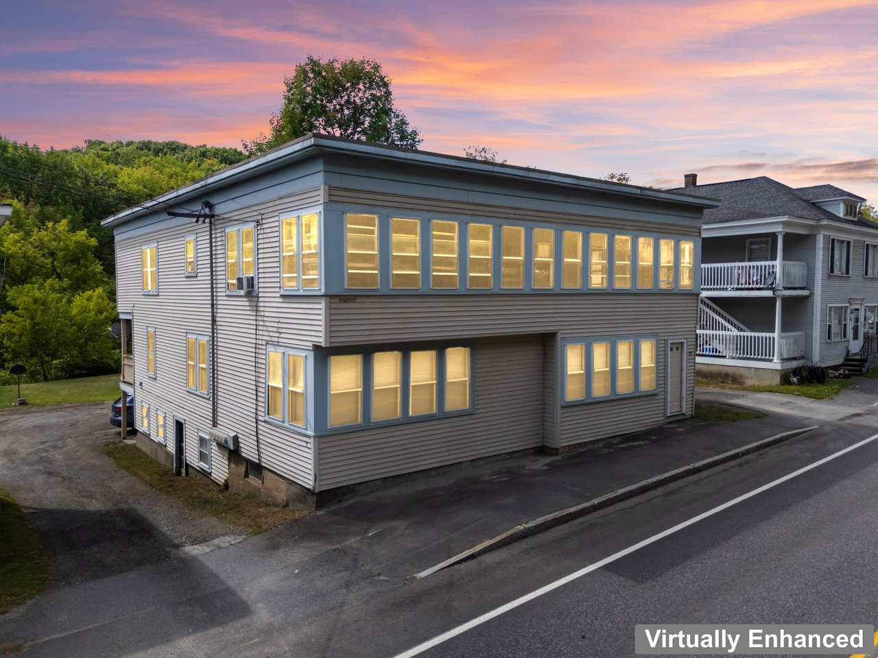 Two-story gray residential building with warmly lit windows at dusk.