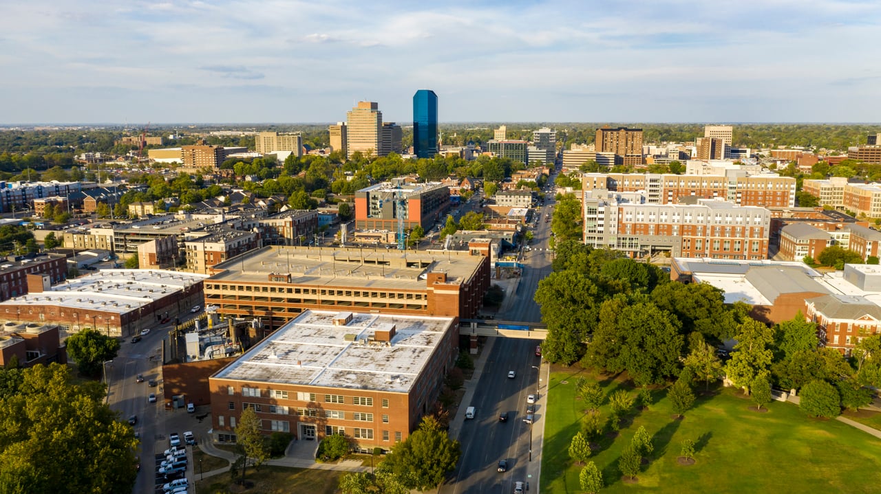Aerial view of downtown with a blue glass tower, tree-lined streets, and a green park.