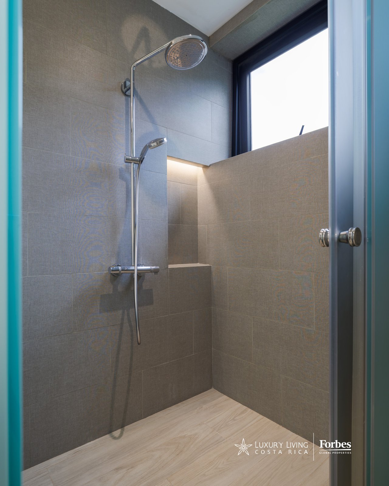 Walk-in shower with gray tile, chrome rainfall showerhead, built-in ledge, and high window.