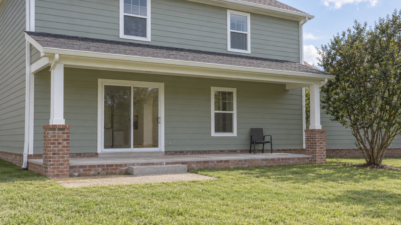 Two-story house with a covered rear patio, sliding glass door, and open lawn.