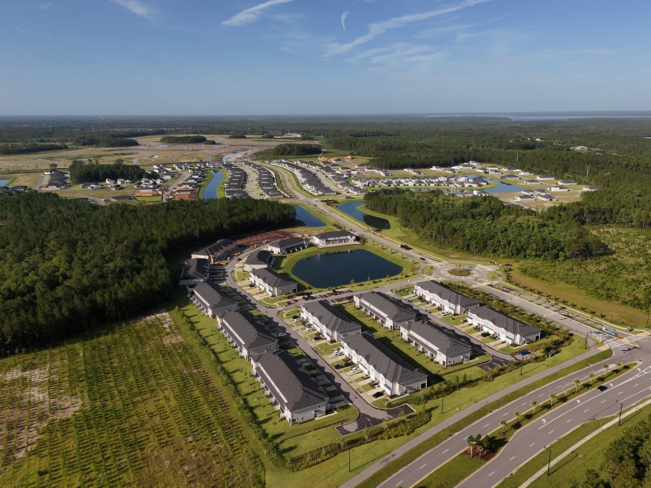 Aerial view of a residential community with rows of homes, ponds, and wooded surroundings.