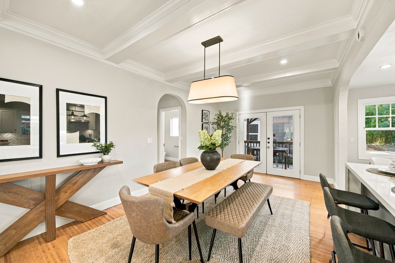 Dining room with a long wooden table, upholstered chairs, coffered ceiling, and French doors.