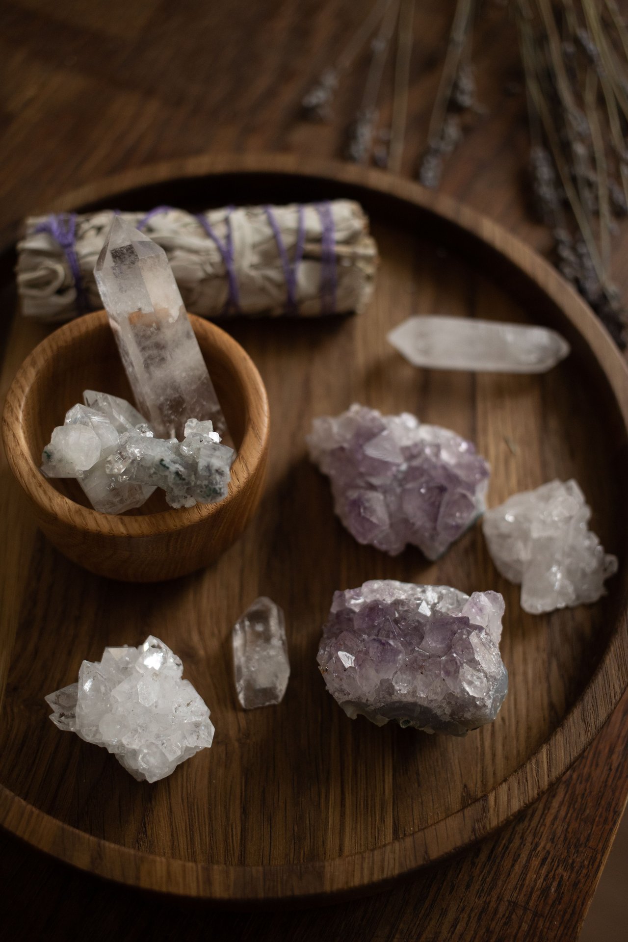 Quartz and amethyst crystals arranged on a wooden tray beside a bundled sage stick.