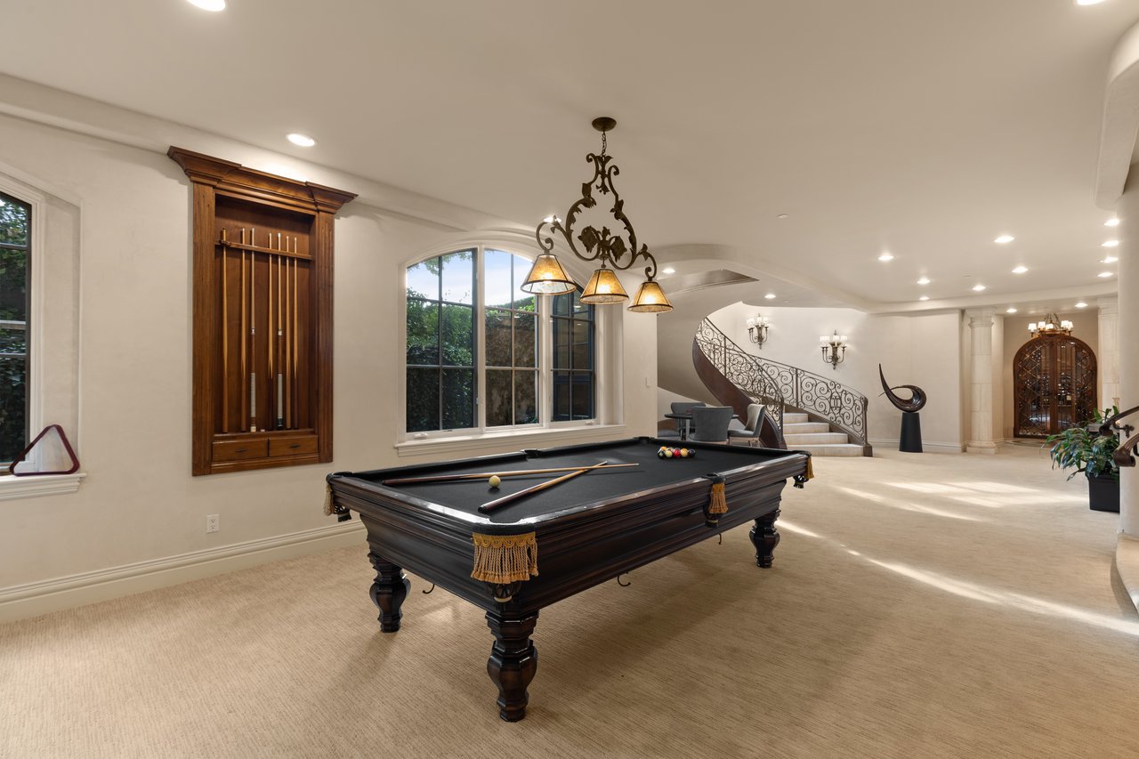 Game room with a dark wood pool table, cue rack, and ornate curved staircase.