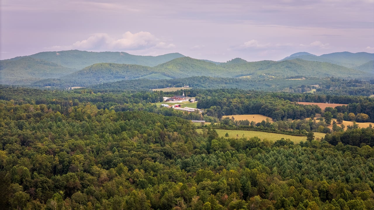 Wooded mountain acreage with open fields and farm buildings in a broad valley.